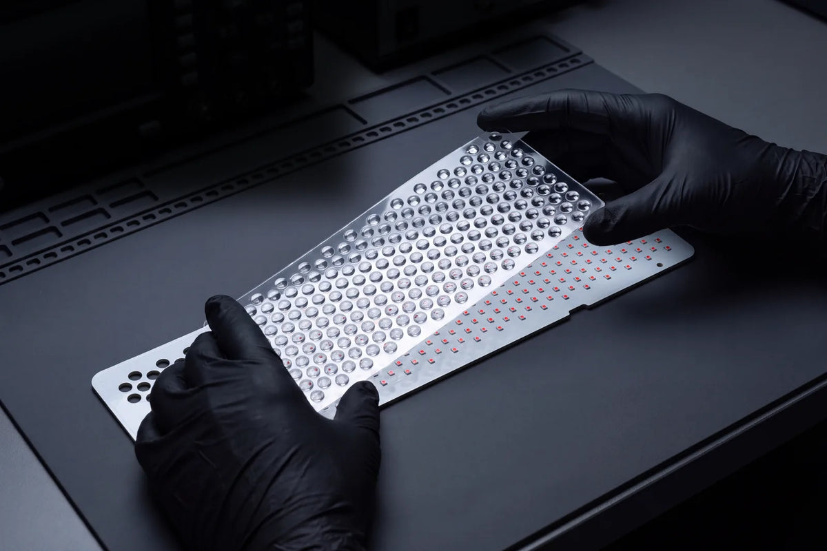 Manos con guantes colocando la lámina de lentes sobre la placa de LED